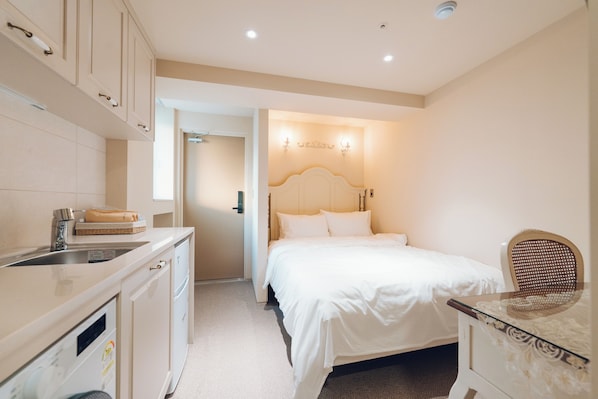 Une chambre à coucher comprenant un lit, une table de chevet et une chaise. On y trouve également une salle de bain avec un lavabo et un miroir. La chambre est décorée dans des tons neutres et présente un design moderne.