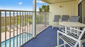 Ein Balkon mit Pool, weißen Stühlen und Blick auf den Strand.