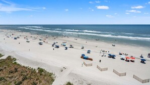 Une vaste plage parsemée de parasols et de chaises longues, un ciel dégagé et l’océan.
