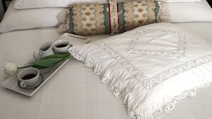 Una cama bien hecha con sábanas blancas, una bandeja con tazas de té y una rosa, y una almohada decorativa.