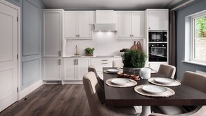 Une cuisine moderne avec des meubles blancs, un four encastré et un coin repas agrémenté d’une table en bois foncé, mise pour quatre personnes.