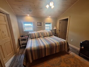 Une chambre à coucher avec un grand lit, deux fenêtres, une table de chevet, une lampe et une commode.