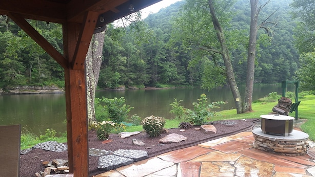 A stone patio with a fire pit and a view of a lake surrounded by trees. - 50 minute ride to the Little League fields (cammal)