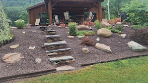 A wooden cabin with a stone pathway leading to the entrance, surrounded by a garden with rocks and plants. - 50 minute ride to the Little League fields (cammal)