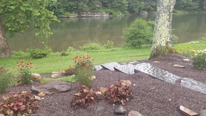 A serene lakeside view with a gravel path, a small garden with red flowers, and a dense forest in the background. - 50 minute ride to the Little League fields (cammal)