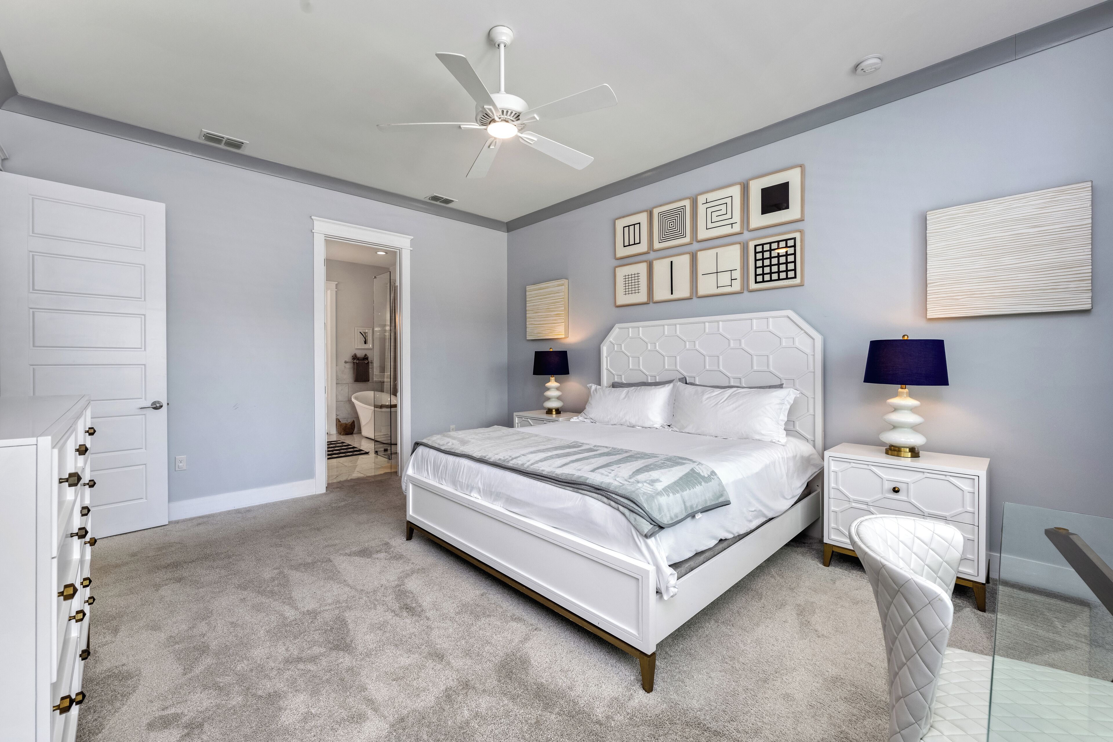Une chambre à coucher comprenant un lit, des tables de chevet, un ventilateur de plafond et des œuvres d’art murales.