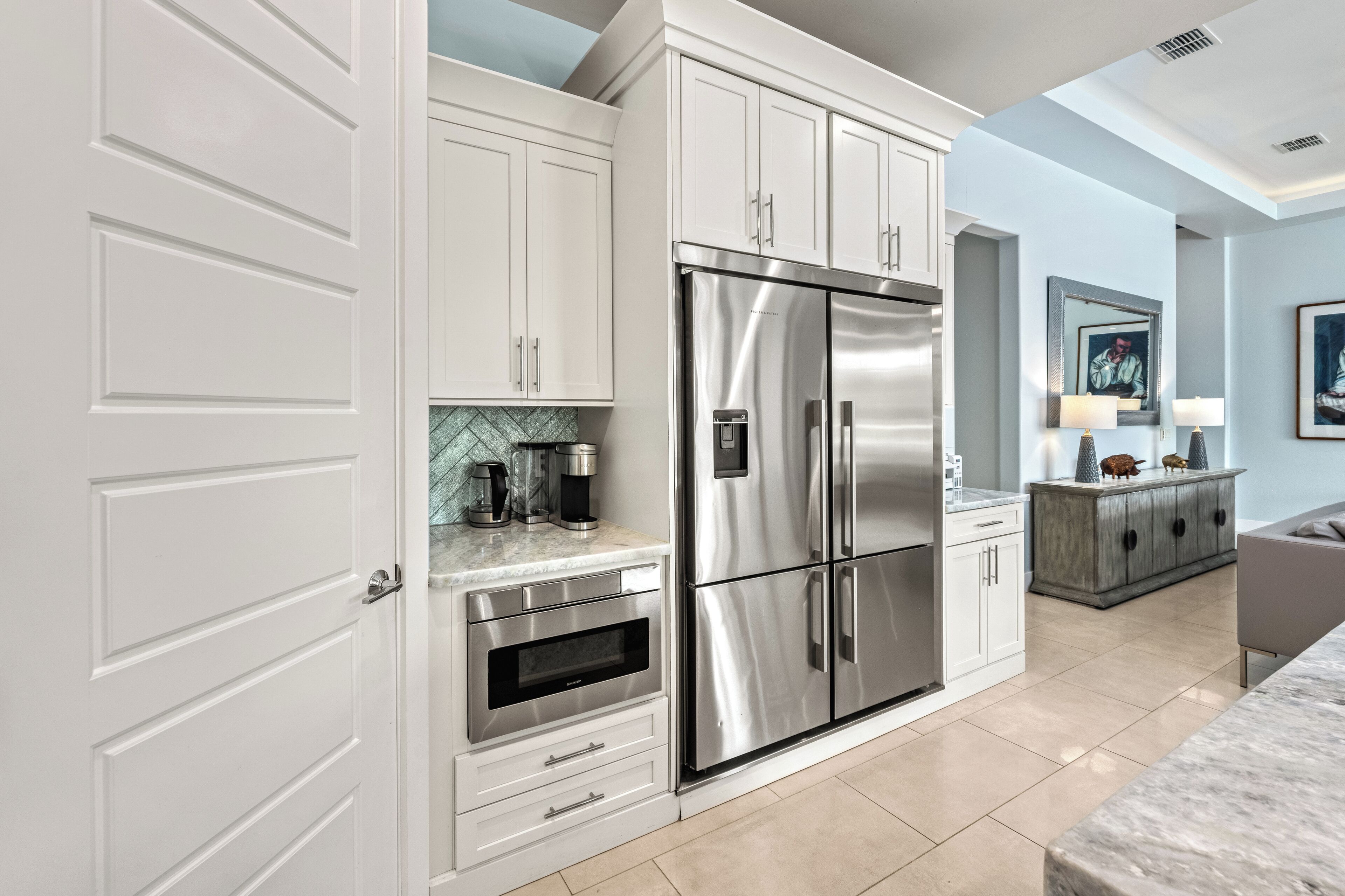 A modern kitchen with white cabinetry, a stainless steel refrigerator, an oven, and a coffee maker.