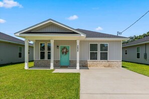 A single-story house with a front porch, a green door, and a brick foundation.