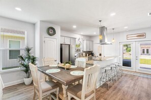 A modern kitchen with white cabinetry, a central island, and a dining area with a wooden table and chairs.