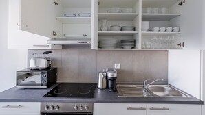Cuina moderna amb forns integrats, cafetera i torradora. Hi ha armaris sobre la barra amb vidrieria i plats.