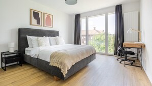 A modern bedroom with a large bed, a desk with a chair, and a view of the city through large windows. - Blueground | Basel-Vorstaedte, view, nr Rhine (Basel)