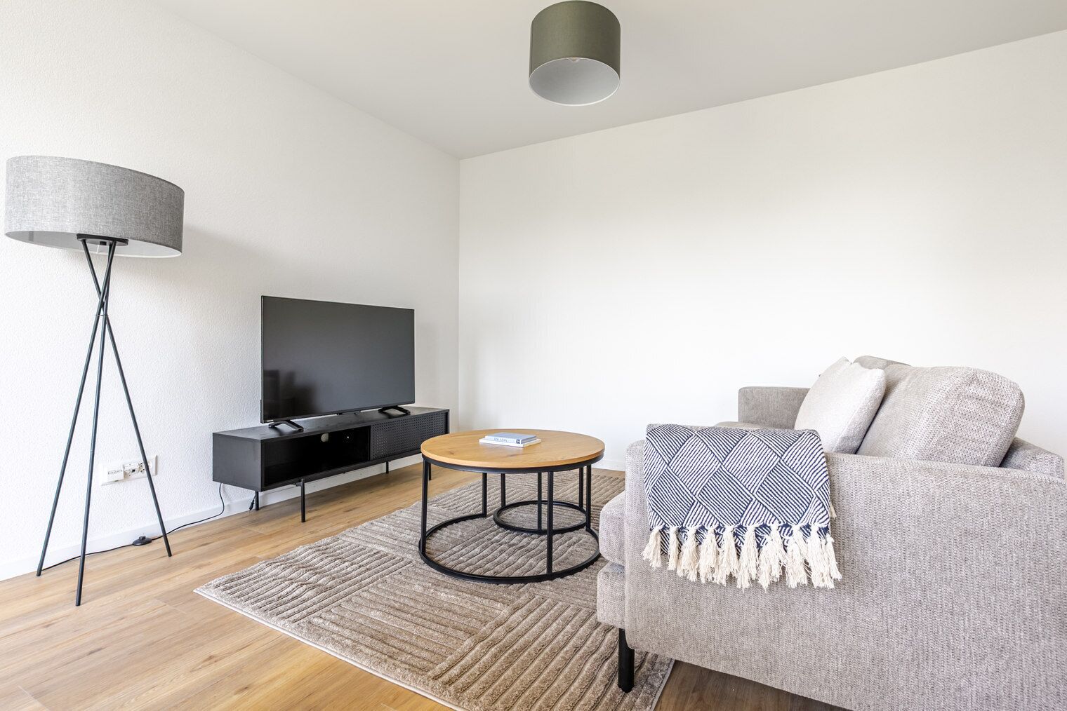 Ein modernes Wohnzimmer mit einem Flachbildfernseher, einem runden Couchtisch, einem grauen Sofa und einer Stehlampe.