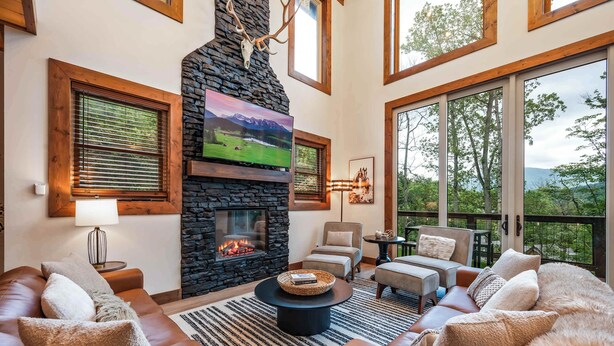 A cozy living room with a stone fireplace, leather sofas, and a large TV. - Luxury Mountain Lodge | Huge Game Room | Htd Pool (Sevierville)