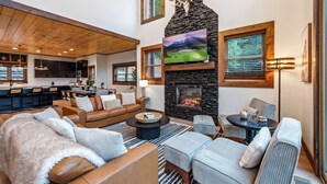 A cozy living room with a fireplace, comfortable seating, and a kitchen area in the background. - Luxury Mountain Lodge | Huge Game Room | Htd Pool (Sevierville)