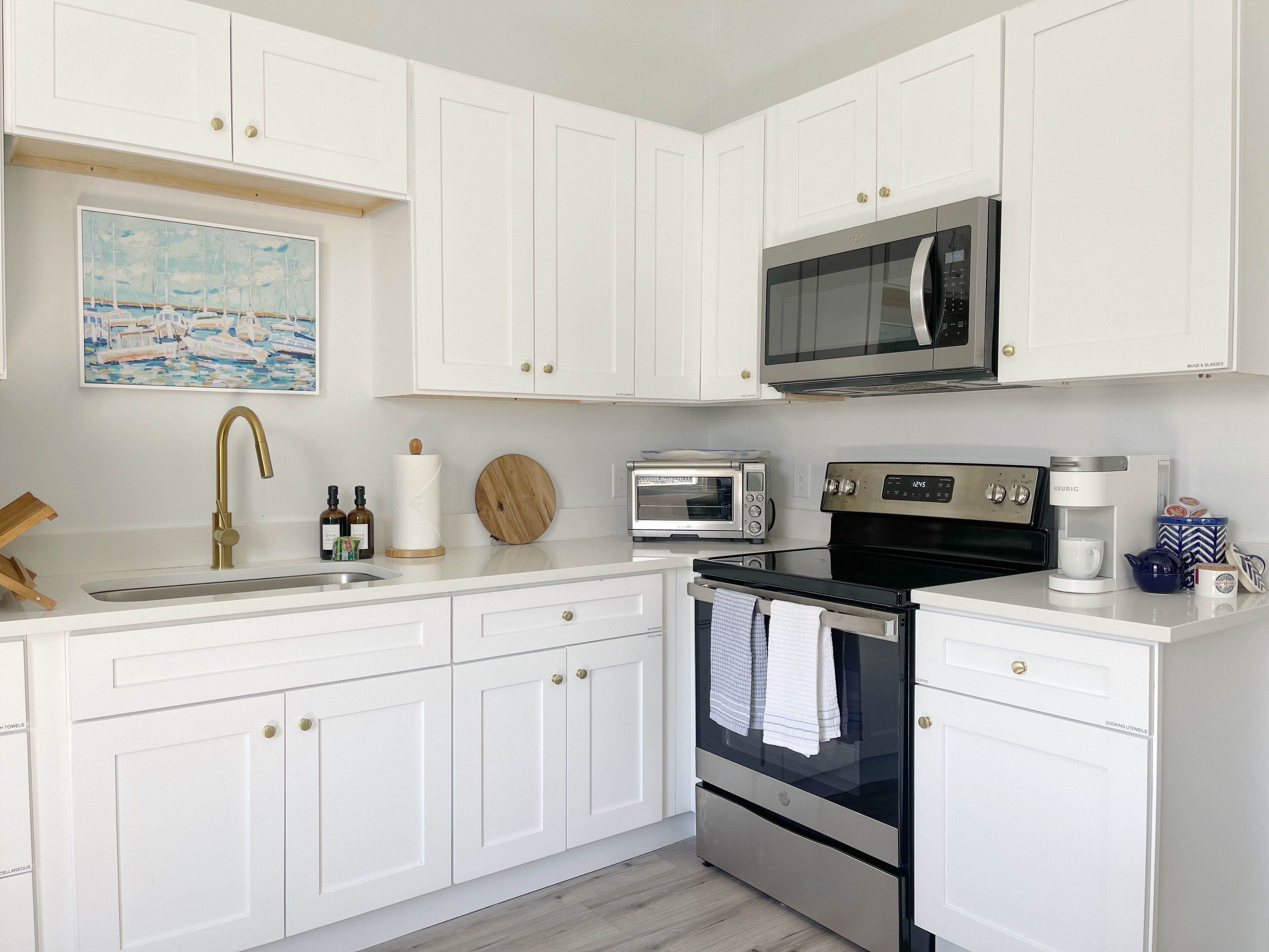 A modern kitchen with white cabinetry, a stainless steel microwave, a built-in oven, a toaster, and a coffee maker.