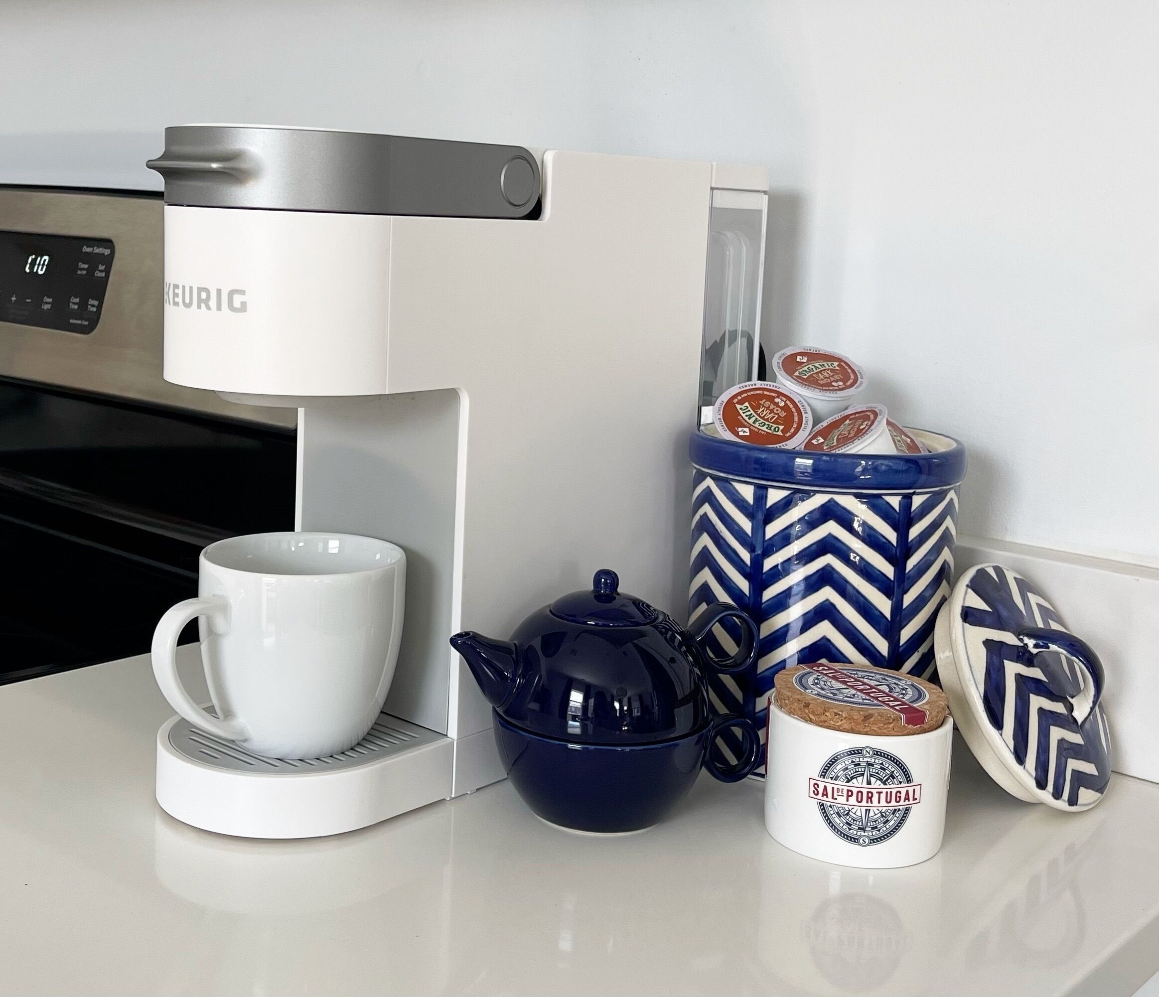 Een koffiezetapparaat, een theepot, een mok en een bakje met theezakjes op een aanrecht.