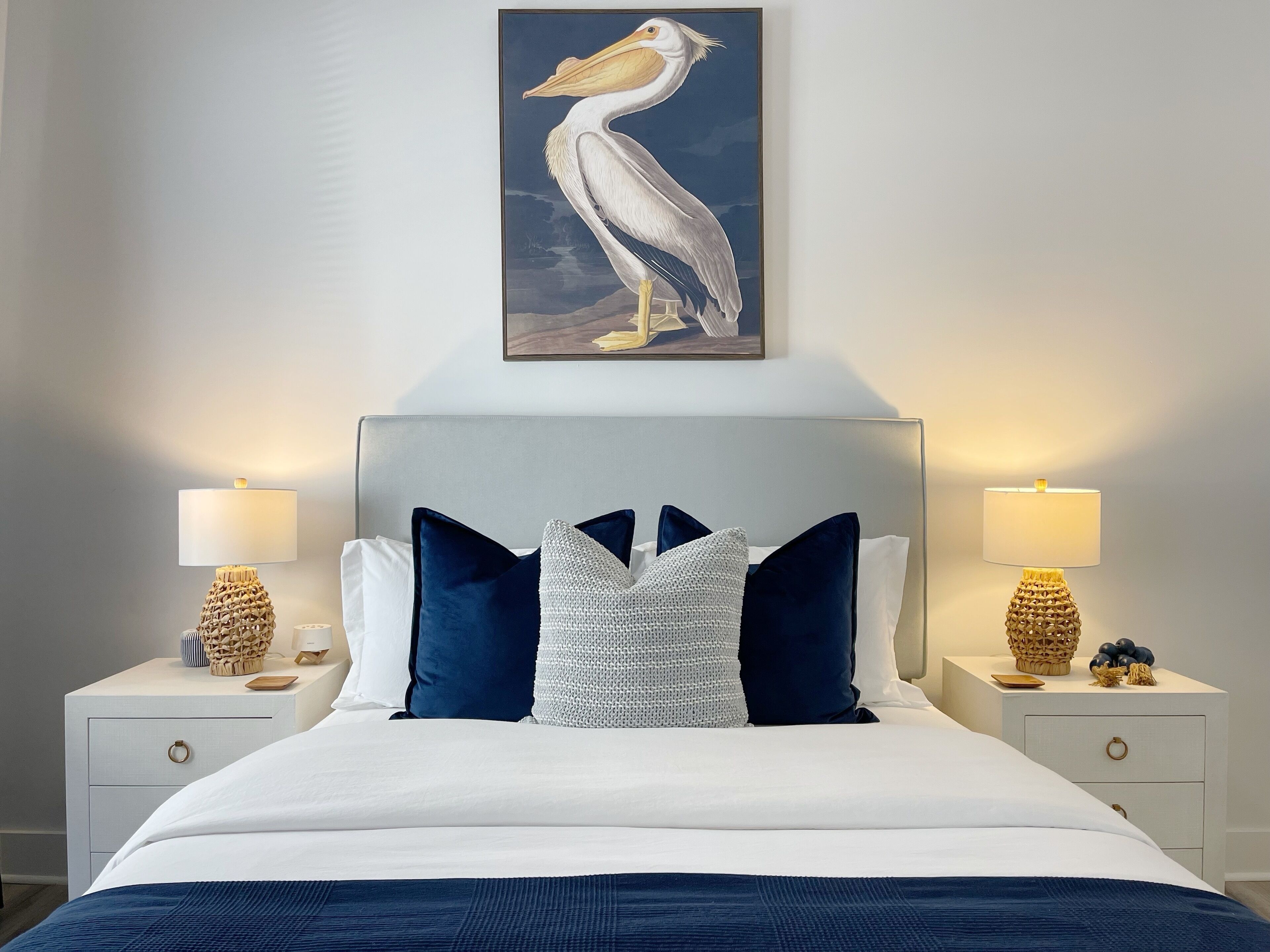 Een net opgemaakt bed met een blauw-witte kleurenschema, met aan weerszijden nachtkastjes, elk met een lamp en decoratieve objecten.