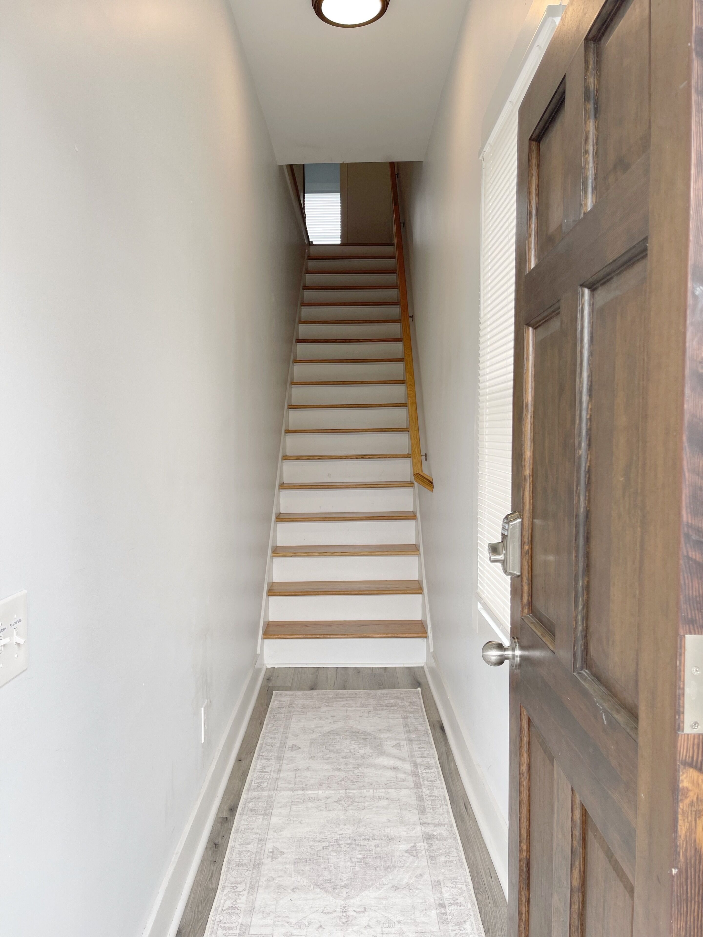 A narrow hallway with a wooden staircase leading to a door with a metal handle.