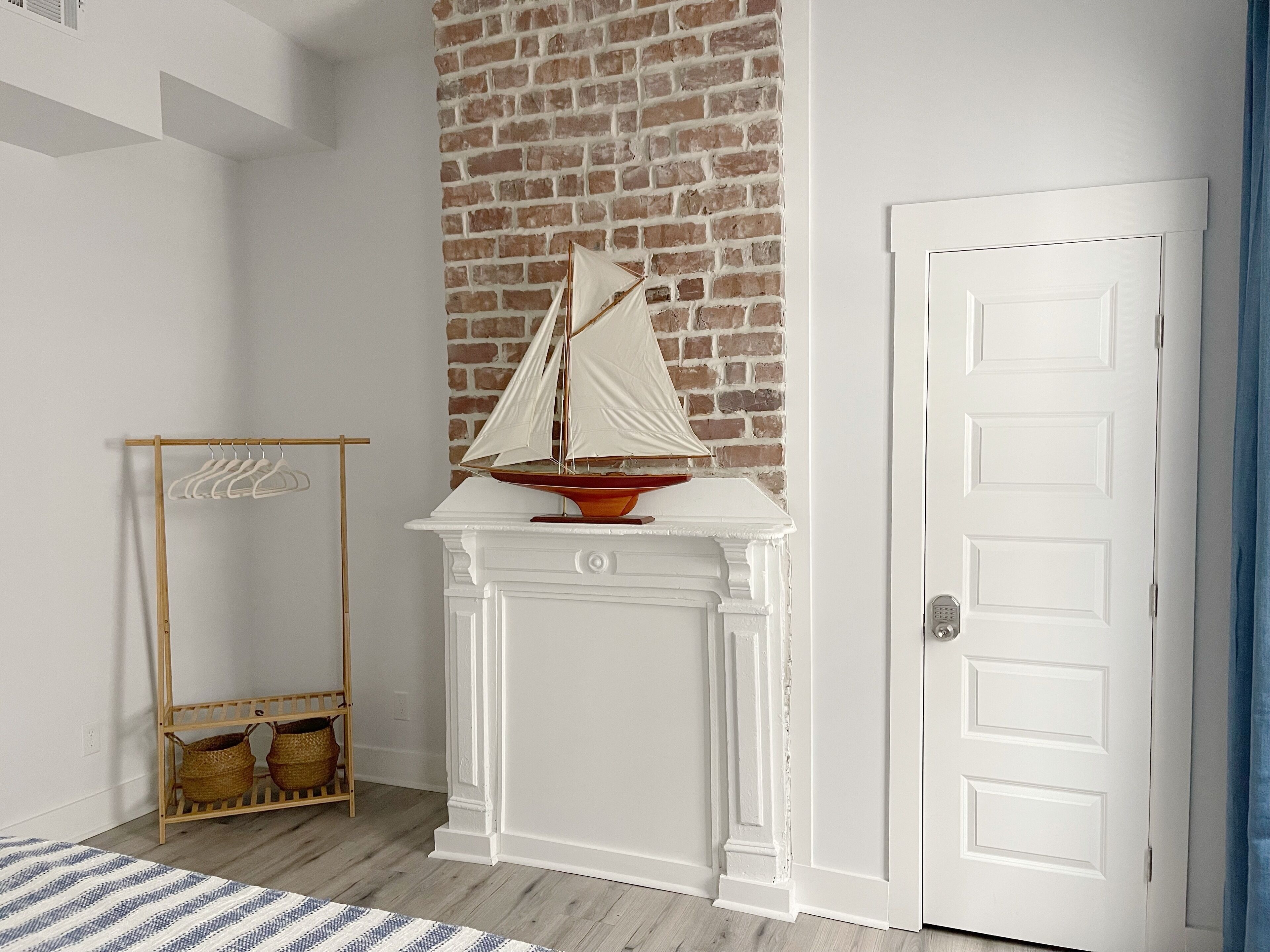 Een kamer met een witte open haard, een bakstenen muur, een houten kapstok en een witte deur.