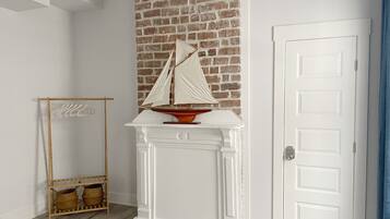 A room with a white fireplace, a brick wall, a wooden coat rack, and a white door.