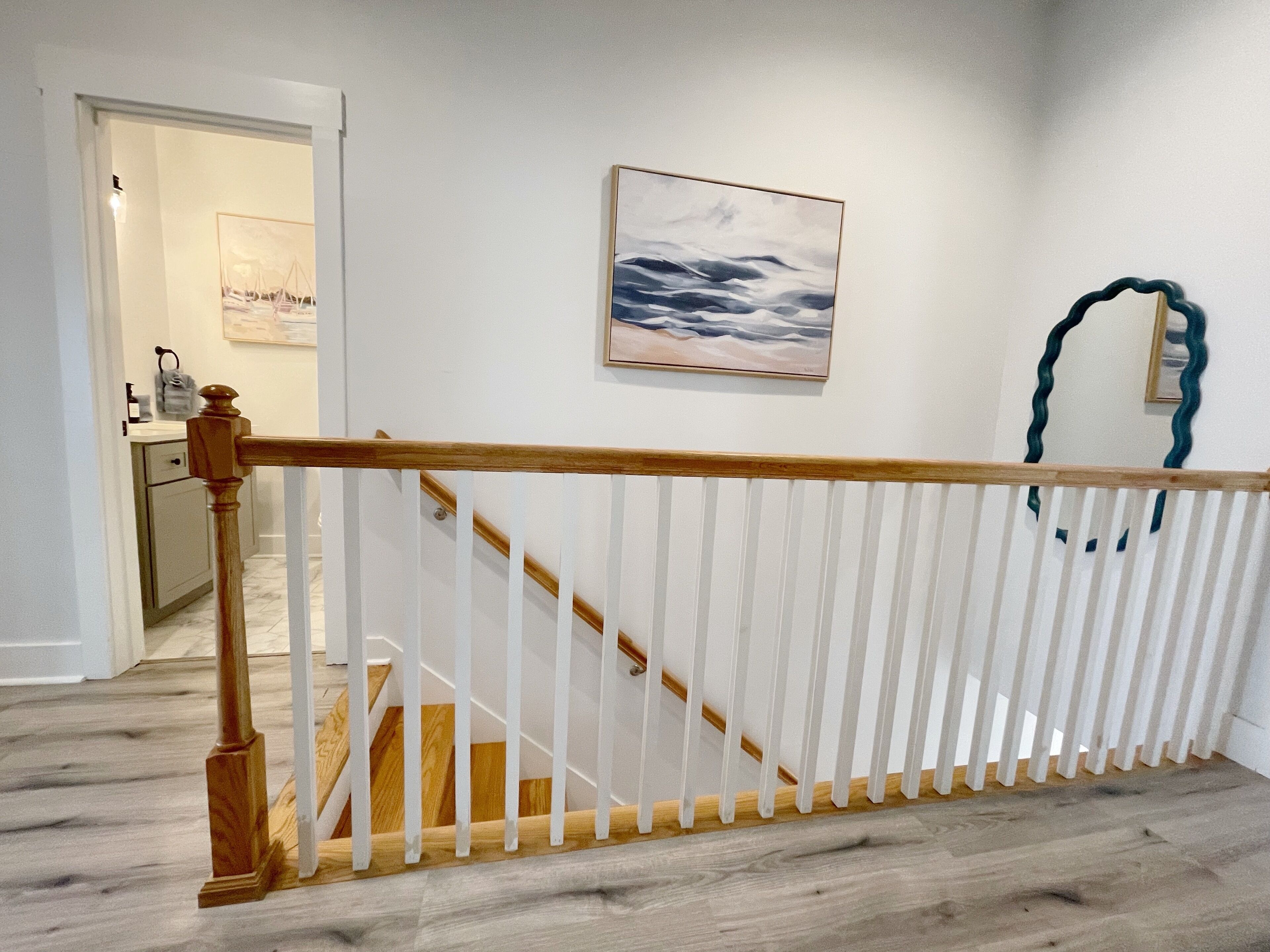 A staircase with white railings and wooden handrails, leading to a landing with a painting of a seascape.