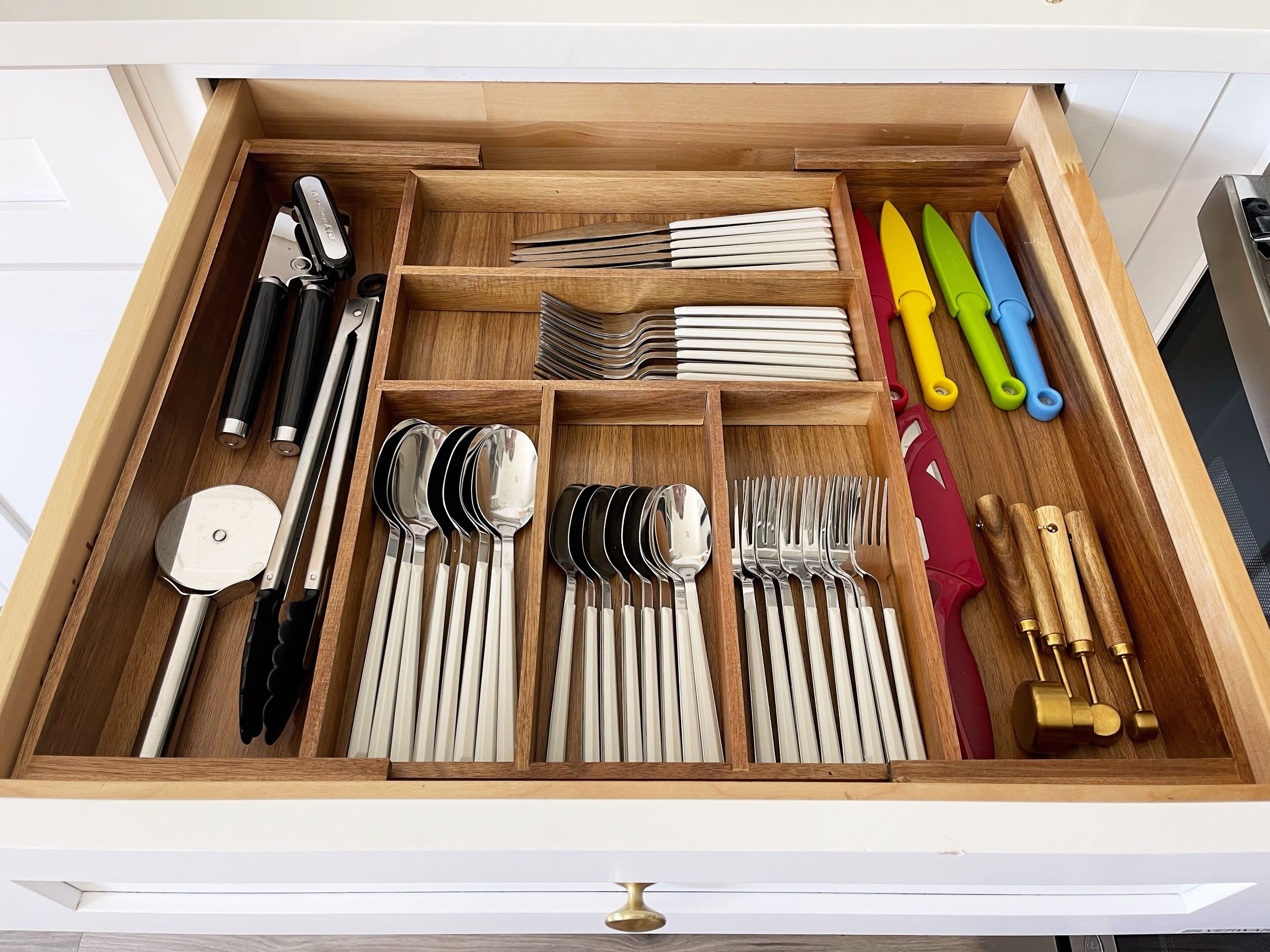 Un cajón con diversos utensilios de cocina ordenados, como cucharas, tenedores, cuchillos y un ablandador de carne.