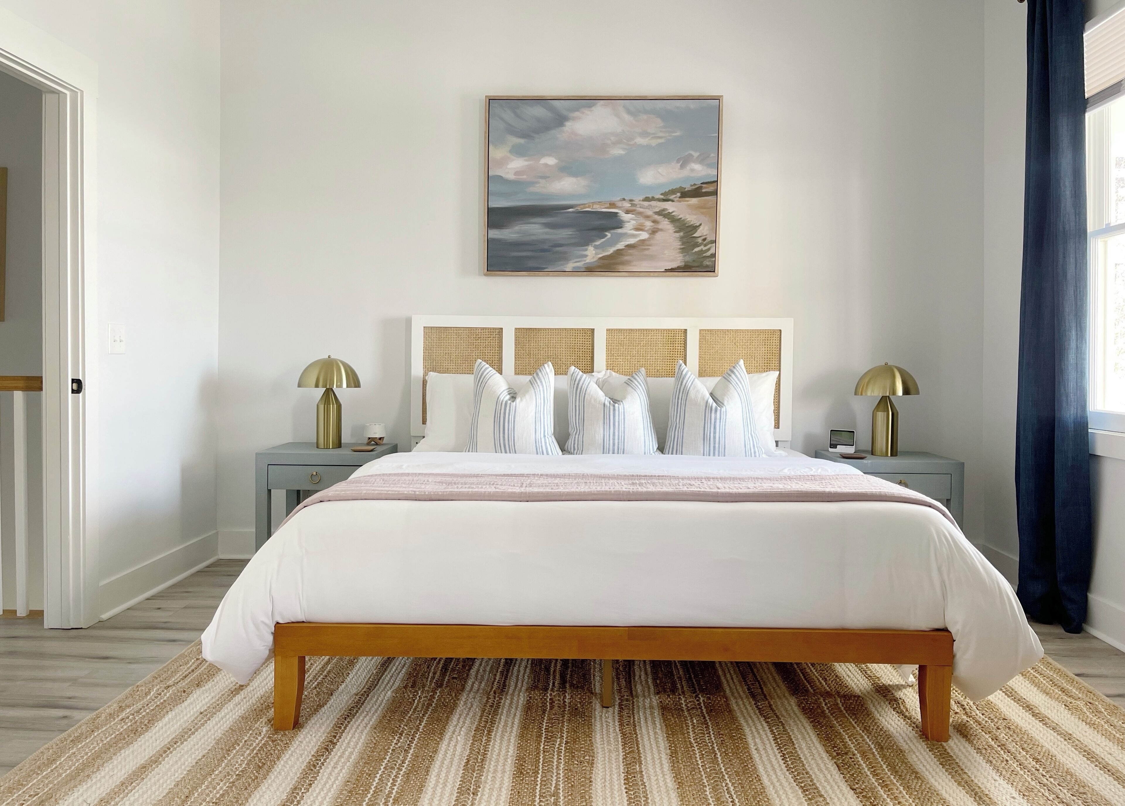 A neatly arranged bedroom with a large bed, two bedside tables, and a painting of a beach scene on the wall.