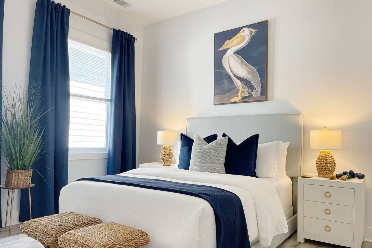 Une chambre à coucher moderne avec un grand lit, deux tables de chevet, une plante en pot et un tableau représentant un pélican.