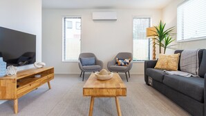 Una sala de estar moderna con una mesa de centro de madera, sillones grises, un sofá gris y un televisor de pantalla plana.