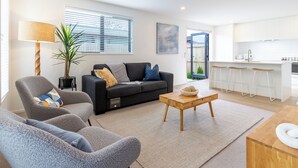 Una sala de estar moderna con sofá, sillones, una mesa de centro y una zona de cocina con taburetes de bar.
