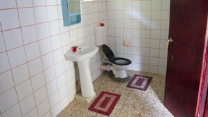 A small bathroom with a white sink, a toilet, and a mirror. There is a red door and a patterned floor. - Korovou Eco Resort (Naviti Island)