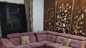 A living room with a sectional sofa, a round ottoman, a ceiling fan, and a decorative wall panel.
