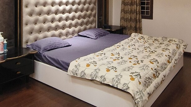 A bedroom with a tufted headboard, a bed with floral bedding, a nightstand, and a ceiling fan.