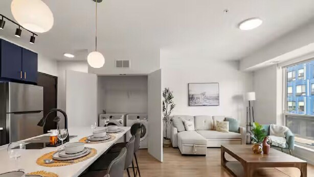 Een moderne keuken met een eetgedeelte, een woonkamer met een bank en salontafel, en een groot raam met uitzicht over de stad.