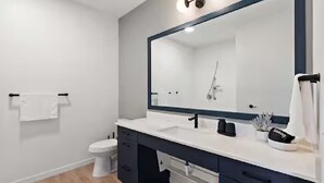 Een moderne badkamer met een wit wastafel, donkere kastjes en een grote spiegel.
