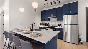 Een moderne keuken met donkerblauwe kastjes, een roestvrijstalen koelkast en een centraal eiland met barkrukken.