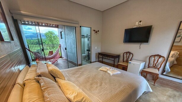 Une chambre avec un grand lit, un bureau, une chaise, une télévision et un balcon équipé d’un hamac.