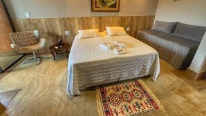 Une chambre à coucher avec un grand lit, un canapé, un fauteuil, une table de chevet et un tableau au mur.