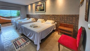 Une chambre d’hôtel avec trois lits, une chaise rouge, un banc en bois et une grande fenêtre donnant sur l’extérieur.