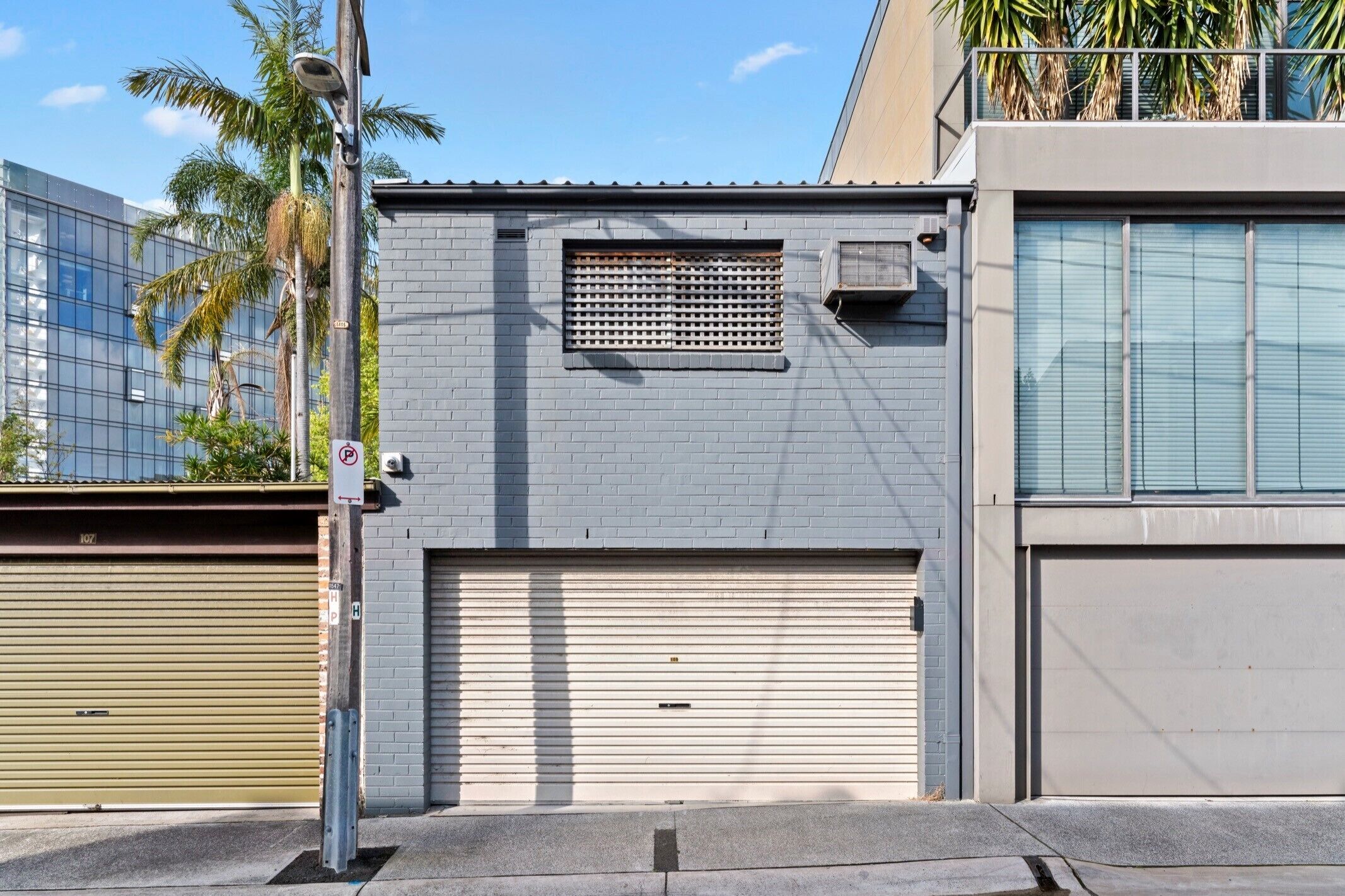 Un bâtiment avec une porte de garage fermée, une caméra de surveillance et un panneau indiquant qu’il est interdit de se garer.