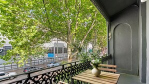 A balcony with a wooden table and bench, a potted plant, and a view of a street with cars and buildings.
