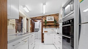 A modern kitchen with white cabinetry, a brick accent wall, and built-in appliances.