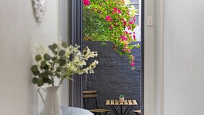 A view through a doorway to an outdoor seating area with a table and chairs, a potted plant, and a black brick wall.
