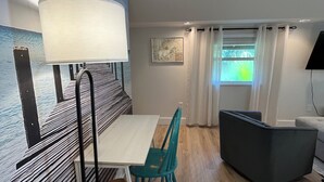 Una habitación moderna con una mesa blanca, sillas color turquesa, un sofá negro, una lámpara de pie y un cuadro abstracto grande en la pared.
