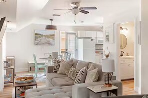 Una sala de estar moderna con un sofá gris, un comedor con mesa y sillas, y una cocina con armarios blancos.