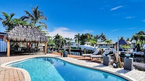 A pool area with lounge chairs, a thatched-roof structure, and boats docked nearby. - Sun-Soaked Retreat with Pool in Pompano Beach (Pompano Beach)