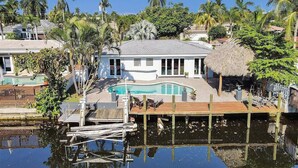 A house with a swimming pool, surrounded by palm trees and a dock extending into a body of water. - Sun-Soaked Retreat with Pool in Pompano Beach (Pompano Beach)