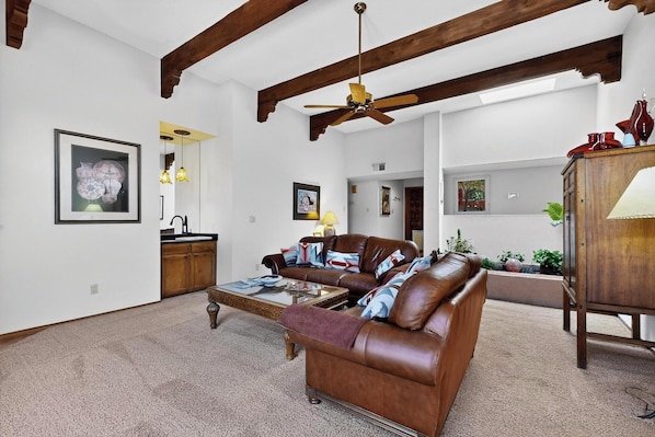 A spacious living room with a brown leather sofa, a coffee table, and a ceiling fan.