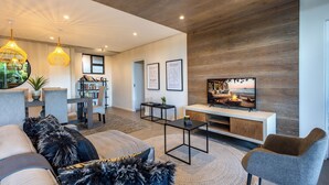 Un salon moderne comprenant un canapé, des fauteuils, une table basse et un téléviseur. On y trouve également une bibliothèque et un mur décoratif en bois.