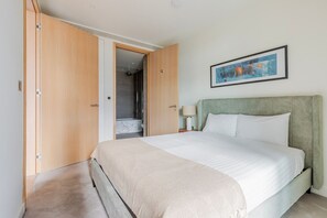 A bedroom with a bed, a nightstand, a lamp, a framed picture, and a walk-in closet. - Blueground | Shoreditch, pool, nr St. Paul's (London)